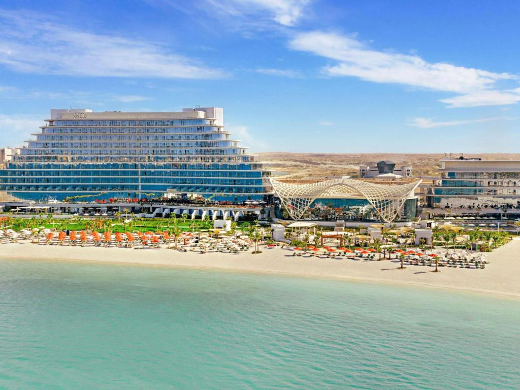 a hotel and a beach with chairs and umbrellas at SO Ras Al Khaimah Hotel & Resort-Ultra All Inclusive in Ras al Khaimah