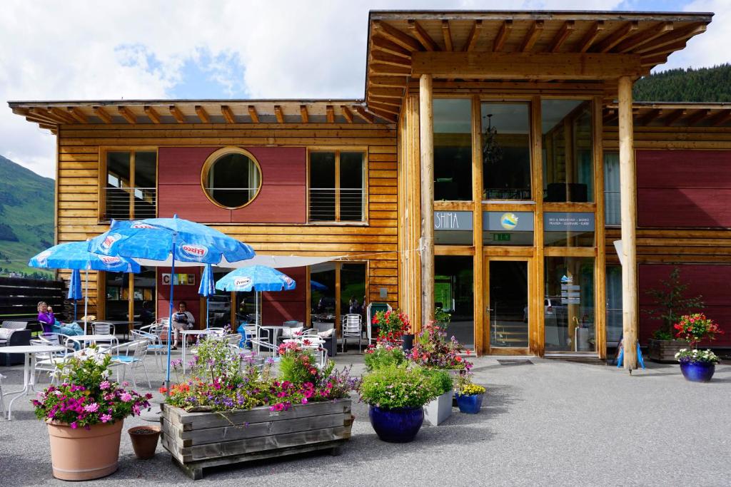 un bâtiment avec des tables, des parasols et des fleurs devant lui dans l'établissement Shima-Davos, à Davos