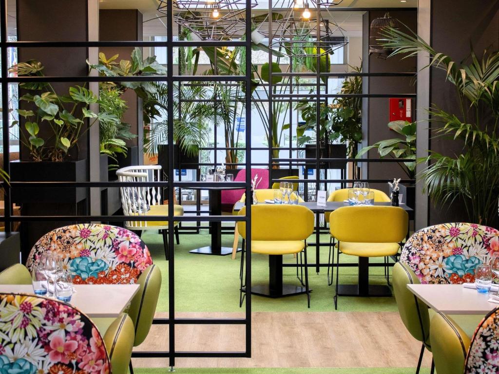 a restaurant with tables and chairs and plants at Hotel Novotel Evry Courcouronnes in Courcouronnes