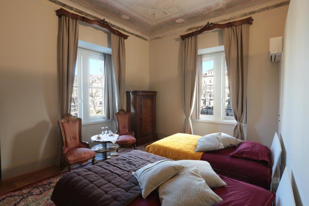 a bedroom with two beds and a table and two windows at Le Saline Luxury Guest House in Trieste