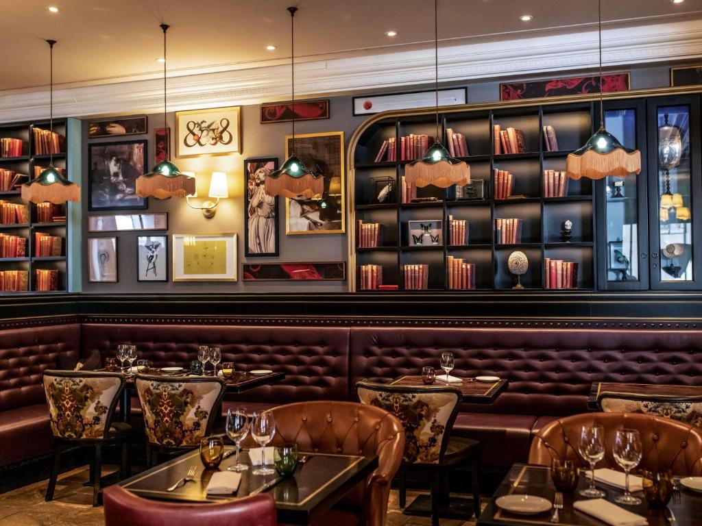 ein Restaurant mit Tischen, Stühlen und Bücherregalen in der Unterkunft Hotel Rotary Geneva - MGallery in Genf