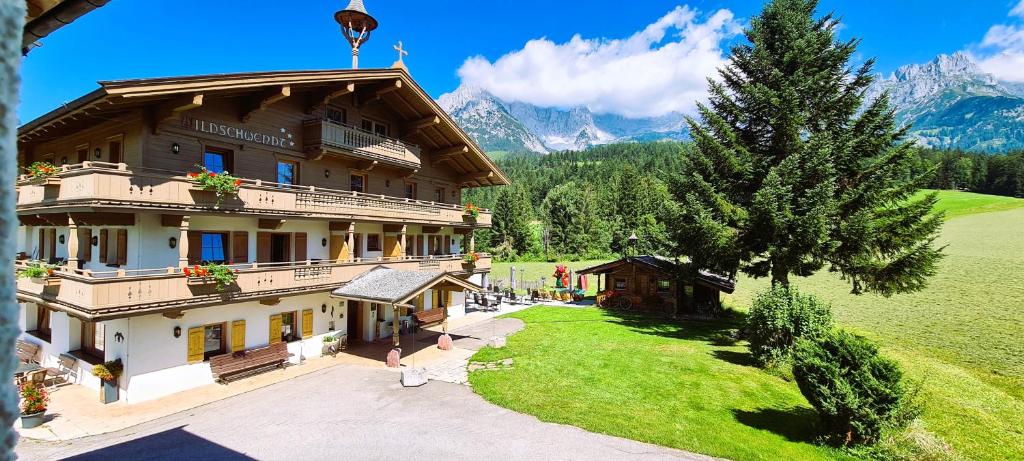 a large building with a tree and mountains in the background at Landhaus Wildschwendt in Ellmau