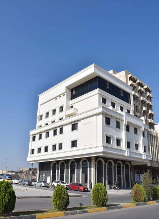 a white building with cars parked in front of it at Al Baron Hotel - فندق البارون in Al Mawşil
