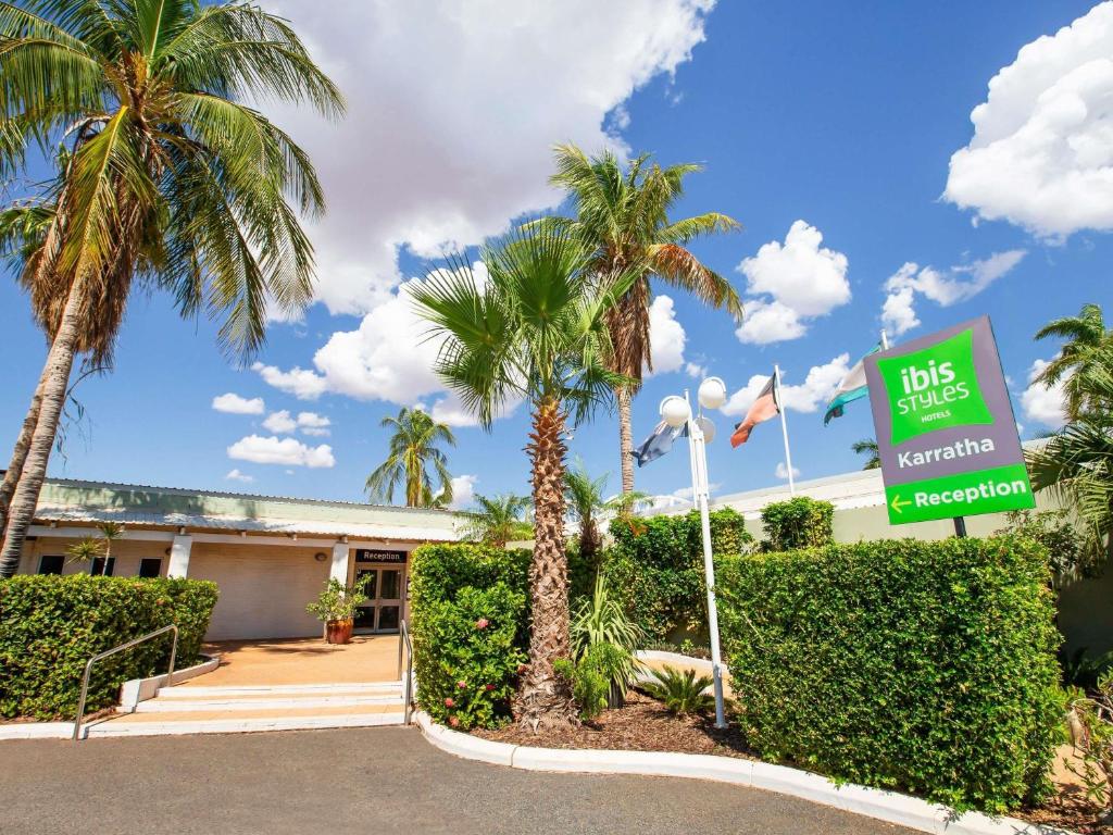 a sign in front of a building with palm trees at Ibis Styles Karratha in Karratha