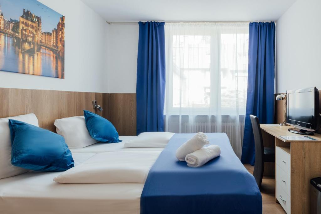 two beds in a hotel room with blue curtains at Hotel Hanseat Hamburg - Free Parking in Hamburg
