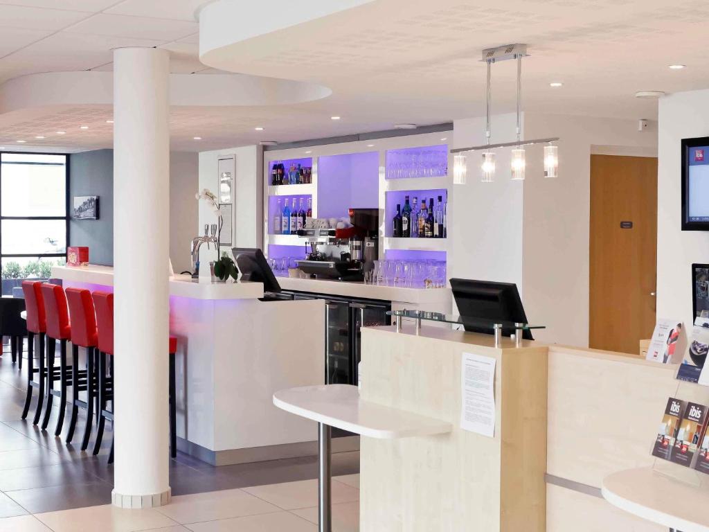 a lobby with a bar with red chairs in a store at ibis Lyon Est Chaponnay in Chaponnay