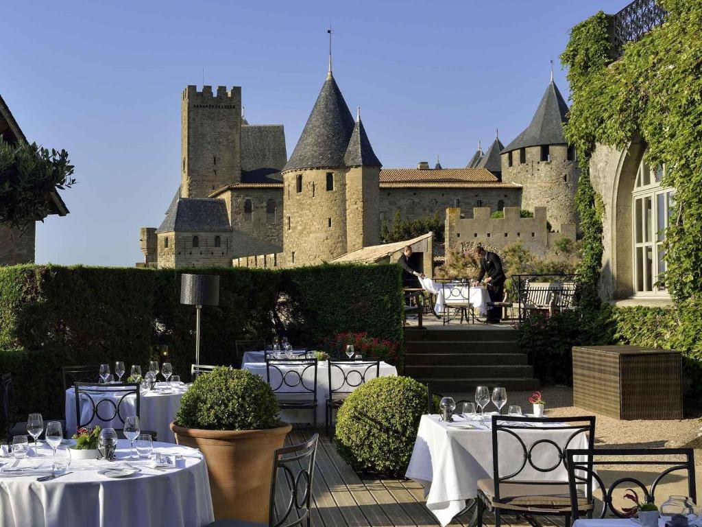 a patio with tables and chairs in front of a castle at Hotel de la Cité Carcassonne - MGallery Collection in Carcassonne