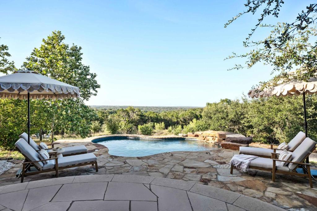 a swimming pool with two chairs and an umbrella at Sunset Ridge Ranch - Pool Outdoor Kitchen & Views in Dripping Springs