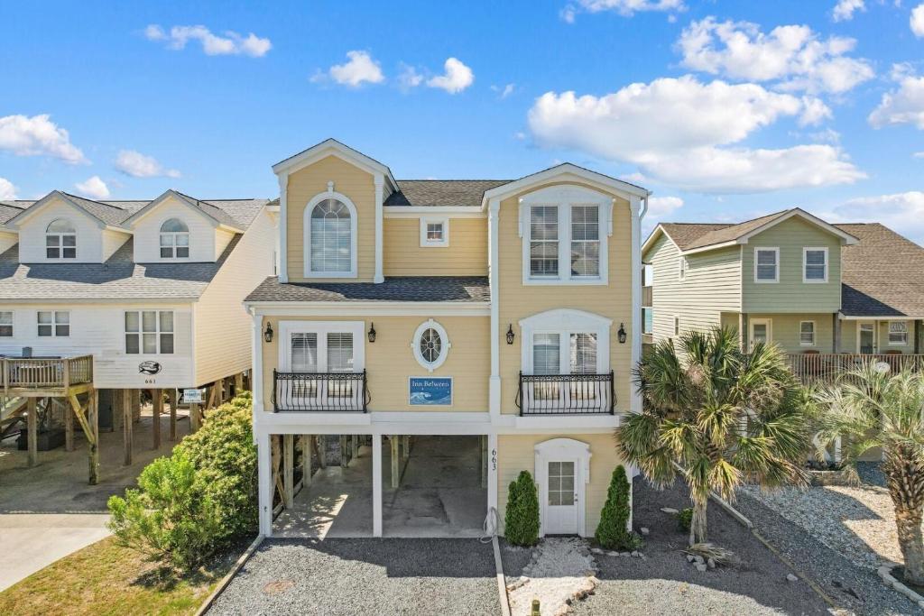 a large yellow house with palm trees in front of it at Inn Between in Holden Beach