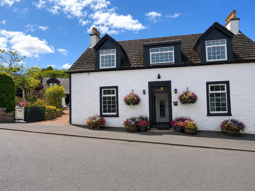 a white house with flowers in front of it at Braeside Guest House, Loch Lomond in Drymen
