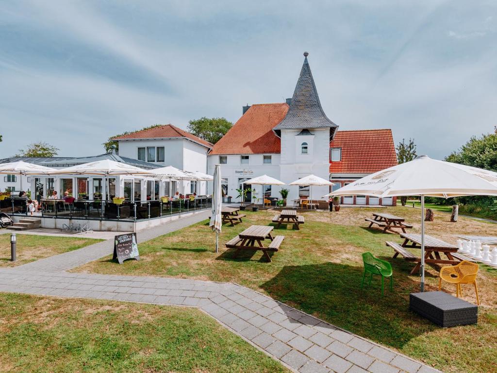 a park with picnic tables and umbrellas in front of a building at Hotel Bloemfontein in Borkum