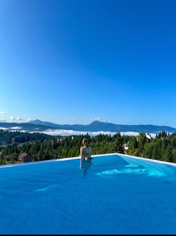 a woman sitting on the edge of a pool with blue water at Шпиці boutique hotel & SPA in Yablunytsya
