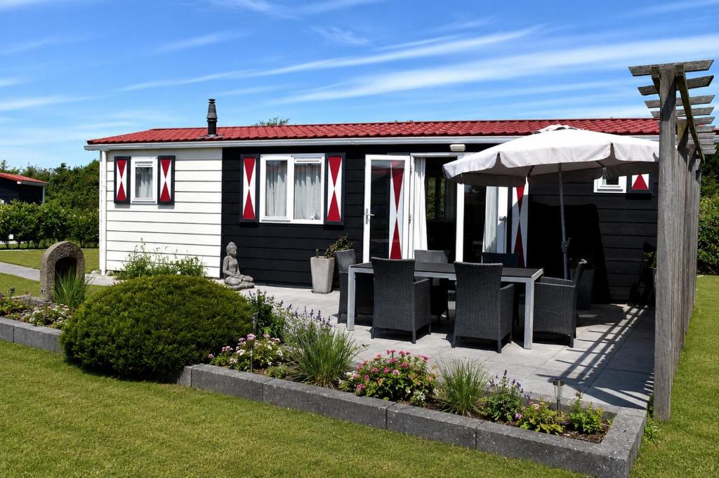 a black and white house with chairs and an umbrella at Chalet dichtbij strand Vrouwenpolder in Serooskerke