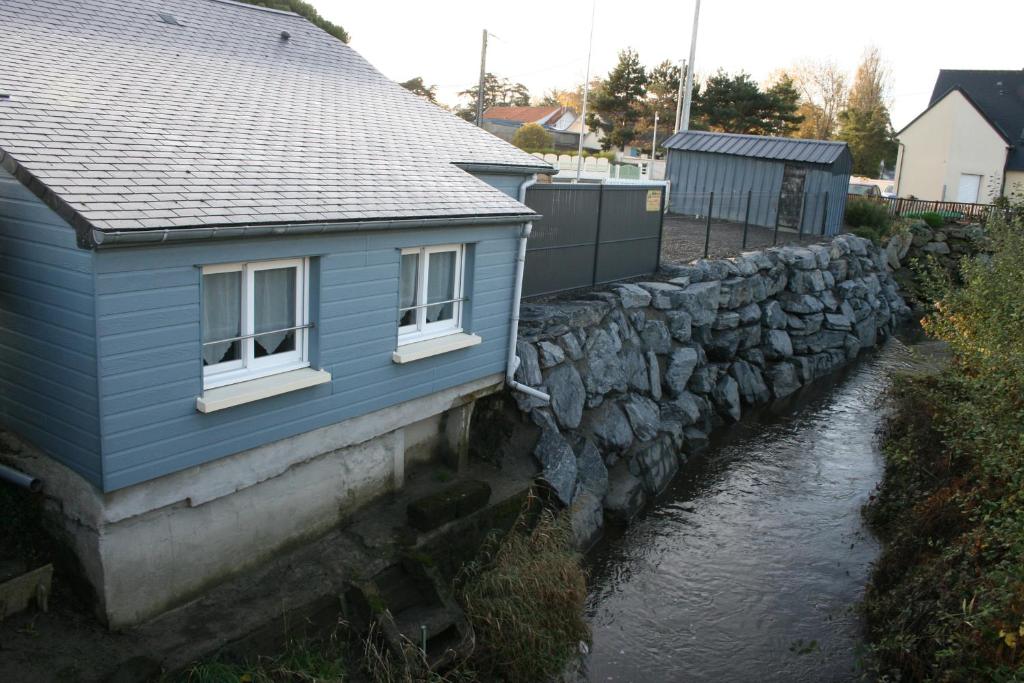 a blue house next to a stone wall next to a river at La Doris gîte de mer in Saint-Pair-sur-Mer