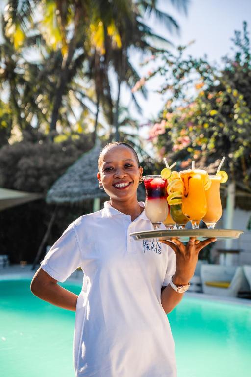 a woman is holding a tray with drinks on it at ZAN Uhuru Beach in Jambiani