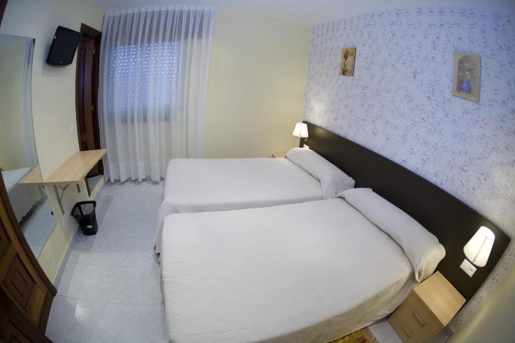 two beds in a hotel room with white sheets at O Cruceiro da Ulla in Vedra