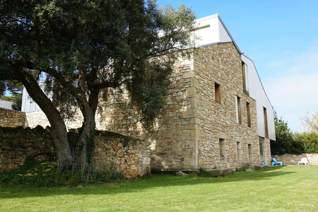 un edificio de piedra con un árbol al lado en The Camp Doniños, en Vila Da Area