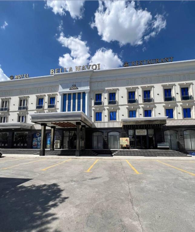 a large white building with a parking lot in front of it at Bella Hotel Navoi in Karmana