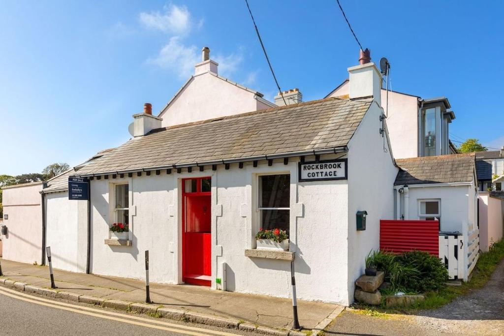 a white building with a red door on a street at Biddy's Cottage Dalkey in Dublin