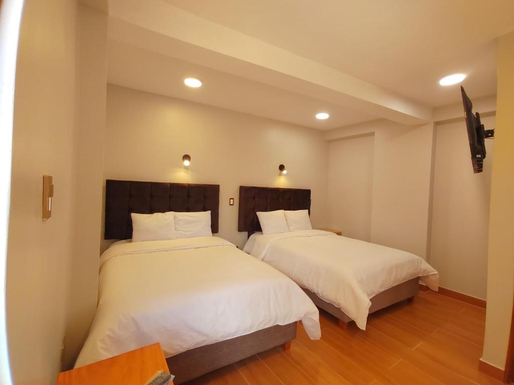 two beds in a room with white sheets at Hotel pumaexplorer in Urubamba