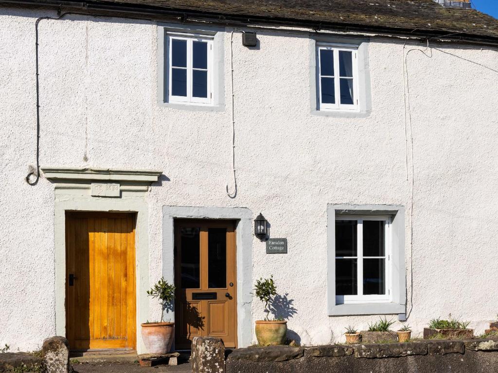 a white house with yellow doors and windows at Earsdon Cottage in Ireby