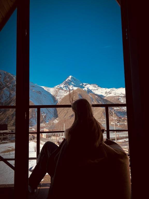 a woman sitting in a window looking at a mountain at Sunset Cottage Kazbegi in Kazbegi