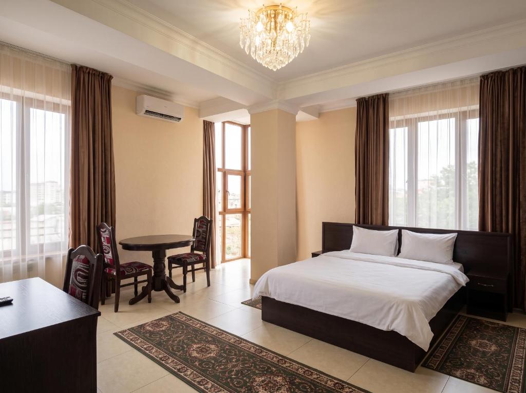a bedroom with a bed and a table and windows at Taugul Hotel in Almaty
