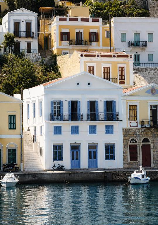a white building with blue doors next to the water at Anamar Symi Residences in Symi