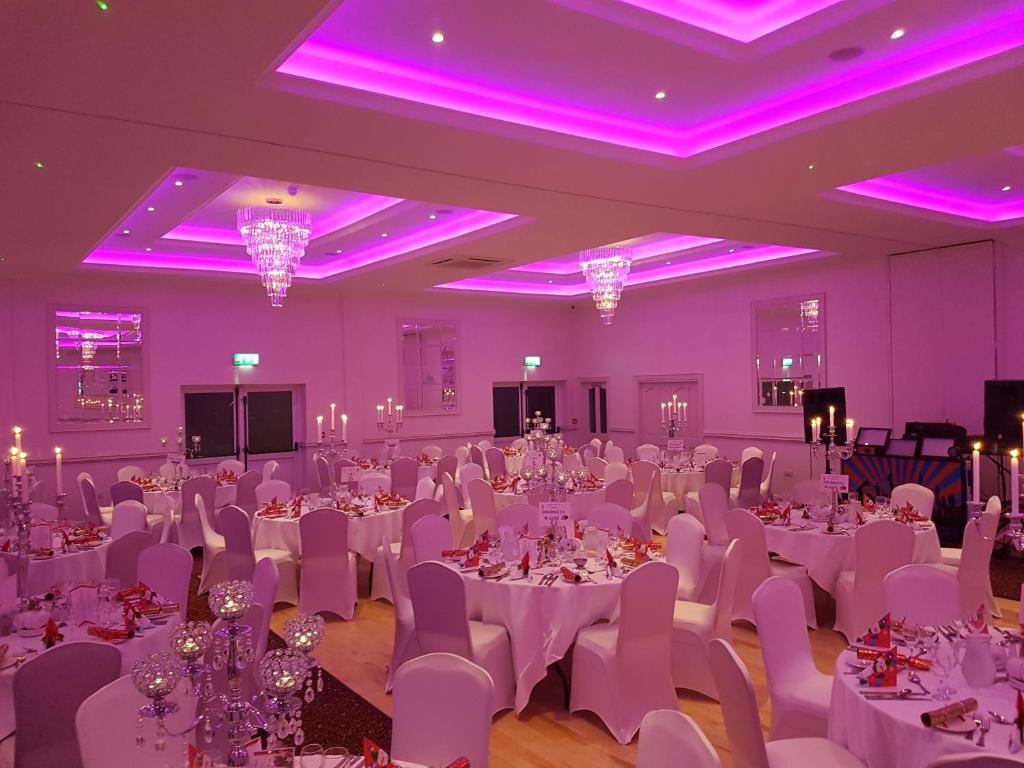 a banquet hall with white tables and chairs and purple lighting at Caisleain Oir Hotel in Annagry