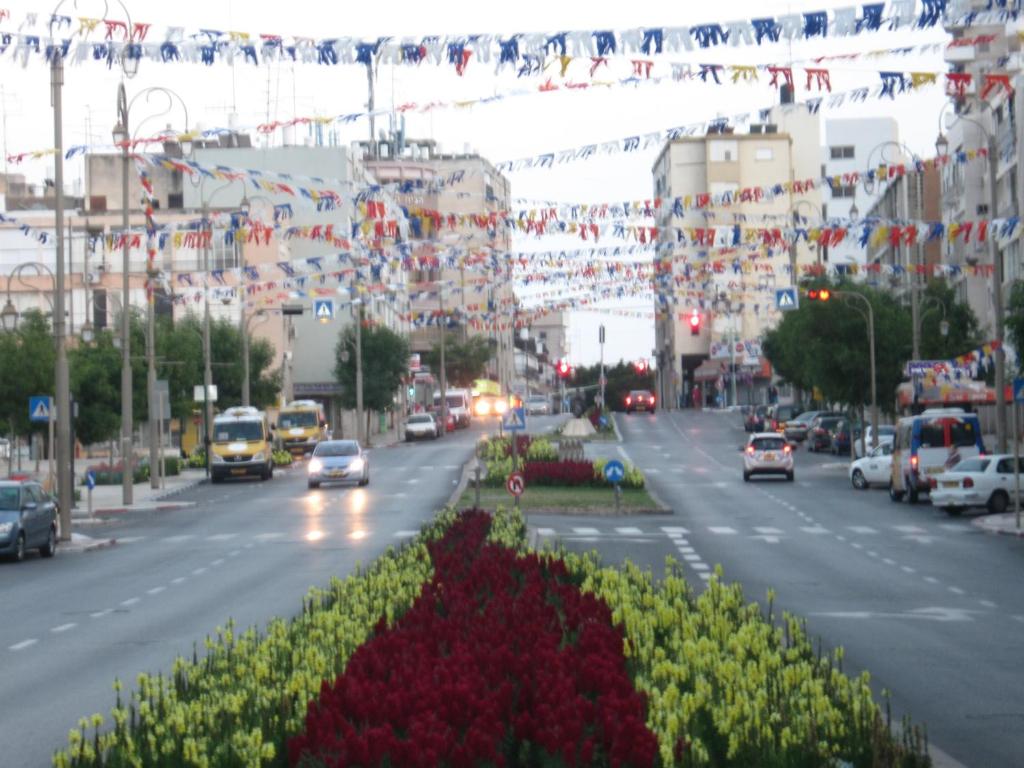 une rue urbaine animée avec des voitures et des drapeaux dans l'établissement Apartments Petah Tiqwa - Bar Kochva Street, à Petaẖ Tiqwa
