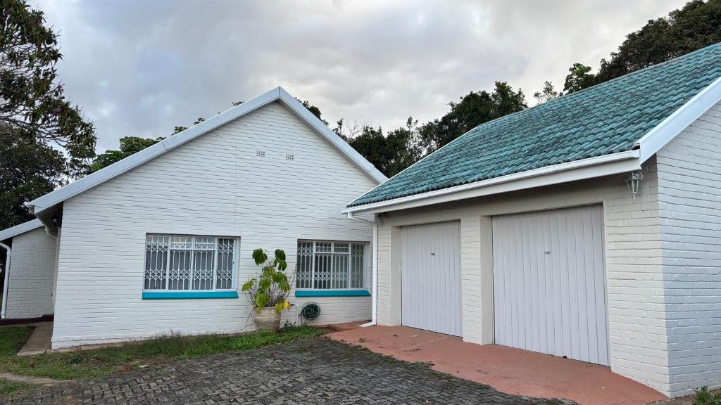 a white house with two garage doors and a tree at 2 bedrooms Ngubelanga Stays in Margate