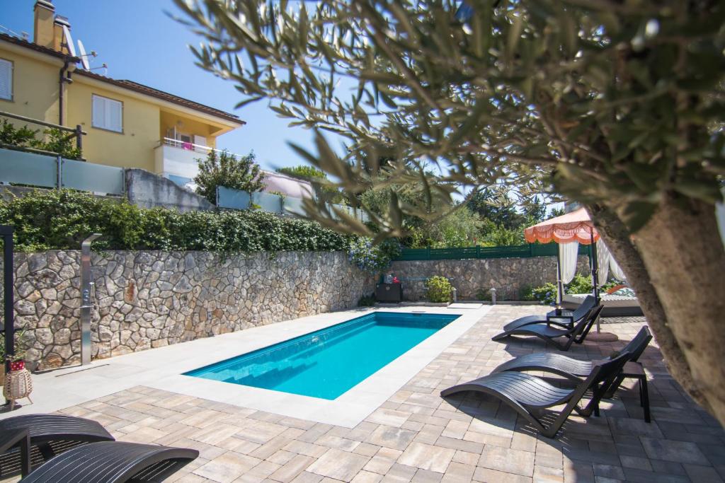 a swimming pool with chairs next to a wall at Apartments Flowers - Heated Pool Near Beach in Krk