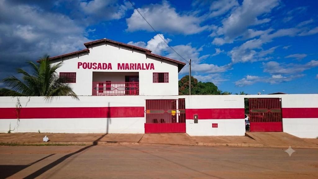 a white building with red doors and a palm tree at Pousada Marialva in Barreiras