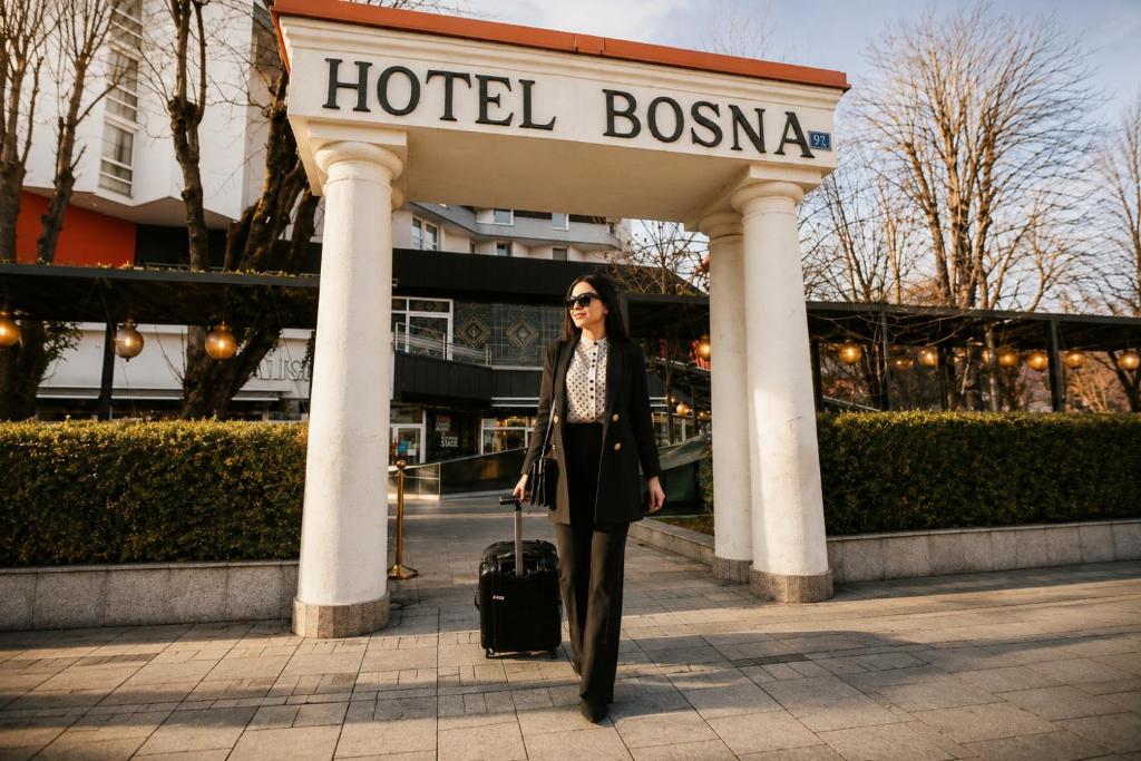 a woman with a suitcase walking under a hotel bosnia sign at Hotel Bosna Banja Luka in Banja Luka