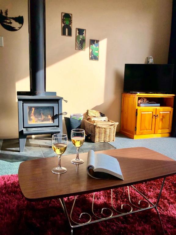 a living room with a fireplace and two glasses of wine at The Shed in Manapouri