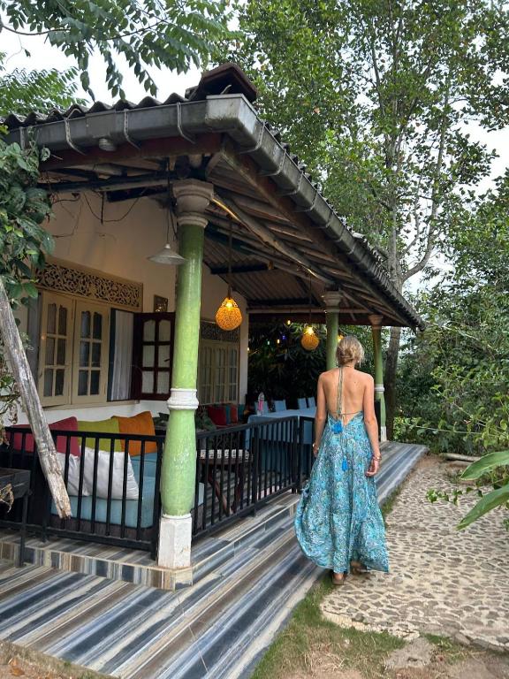 a woman in a dress standing on the porch of a house at Tunnel Gap Homestay in Ella