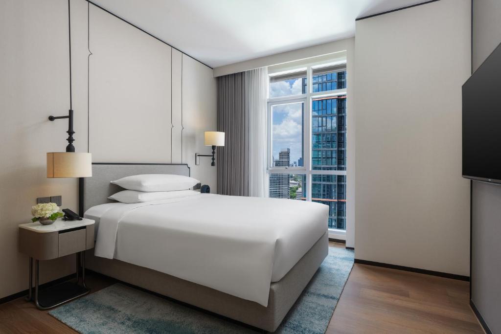 A bright bedroom with a large bed, corner window and wall-mounted television.