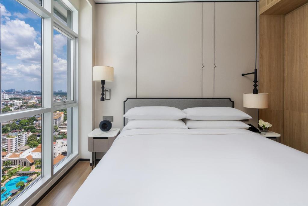 A bed positioned beside floor-to-ceiling corner windows overlooking the city.