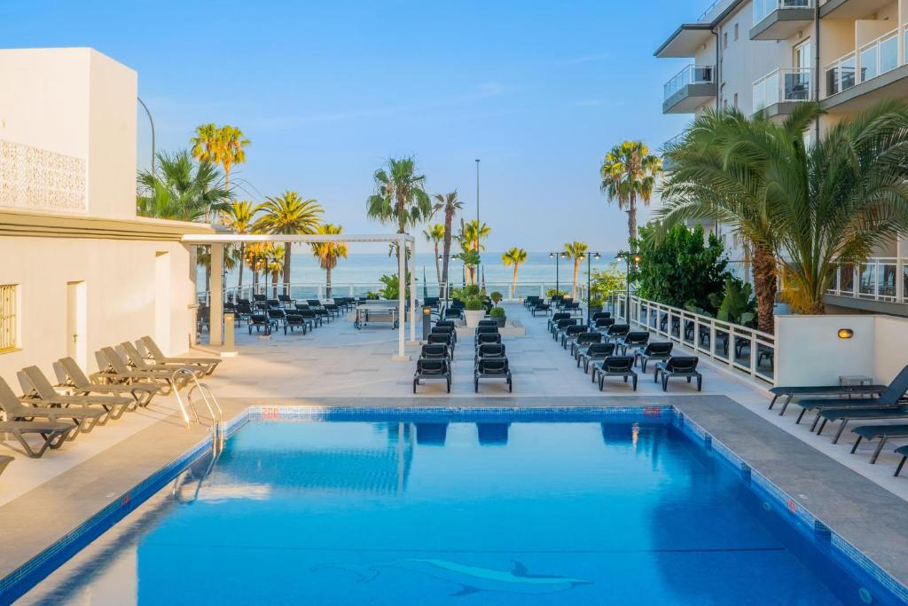 a swimming pool with chaise lounge chairs and the ocean at Hotel Las Arenas, Affiliated by Meliá in Benalmádena
