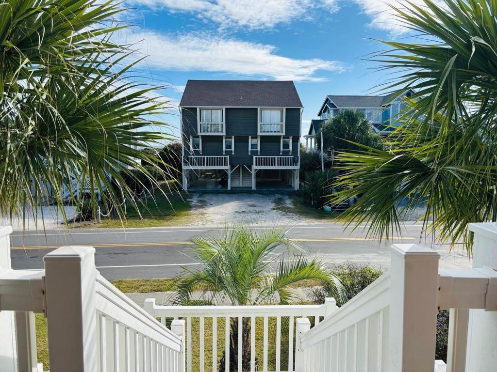 a house with a white fence and palm trees at Beach Ya There in Holden Beach