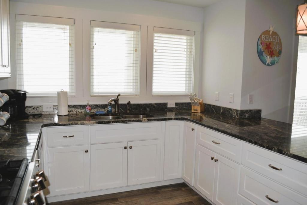a kitchen with white cabinets and a sink and windows at Nautilus Home in Holden Beach