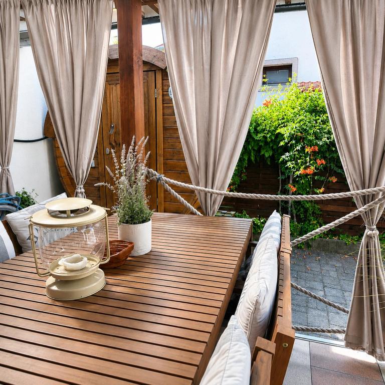 a wooden table on a patio with curtains at Dora Holiday House & Apartments -Sauna & Relax by the Lake in Keszthely