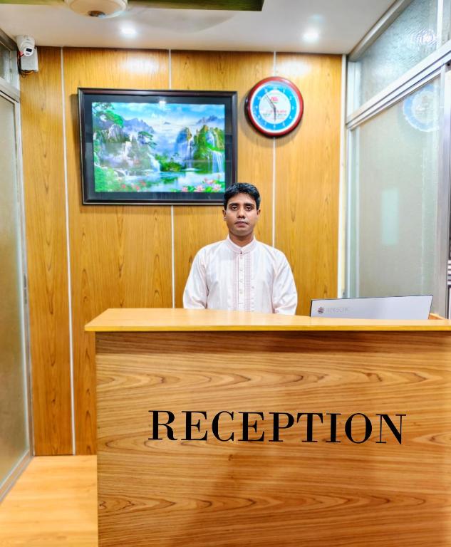 a man is sitting at a reception desk at Ast Guest House in Dhaka