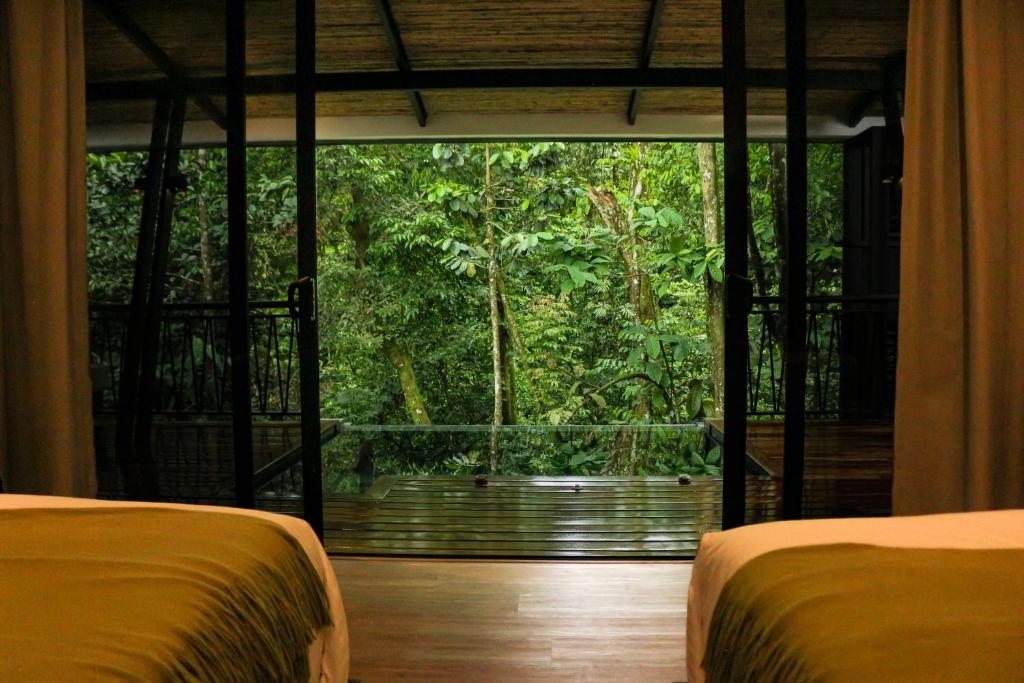 two beds in a room with a view of a forest at Nuakú Jungle in Aguas Zarcas