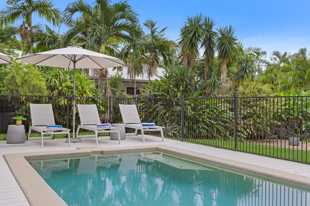 a swimming pool with two chairs and an umbrella at Palm Cove Retreat I heated pool I Family home in Palm Cove