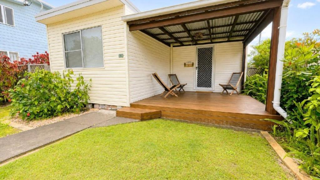 a porch with two chairs on a wooden deck at Teke Cottage in Wooli