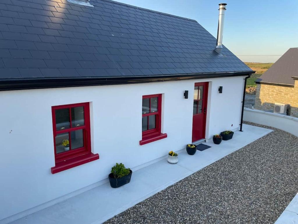 a white house with red windows and potted plants at Dun Aengus Cottage on the Cliffs of Moher in Liscannor