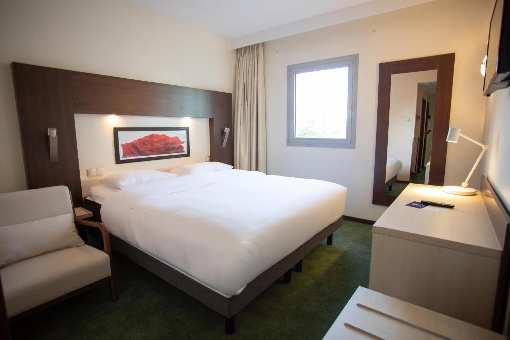 a hotel room with a large bed and a chair at Elema Hotels Beauvais ex Hostellerie Saint Vincent Beauvais Aeroport in Beauvais
