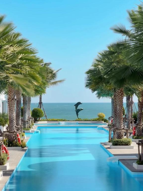 a swimming pool with palm trees in front of the ocean at The Delfini Hua Hin in Hua Hin