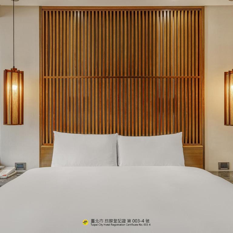 a bedroom with a white bed and a wooden headboard at Guide Hotel Taipei Bade in Taipei